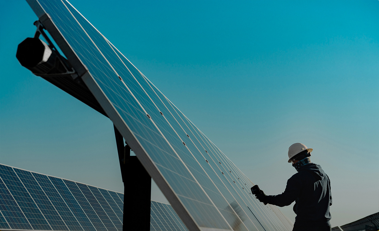 Ein Mann mit Schutzhelm arbeitet an einer grossen Solaranlage im Freien.