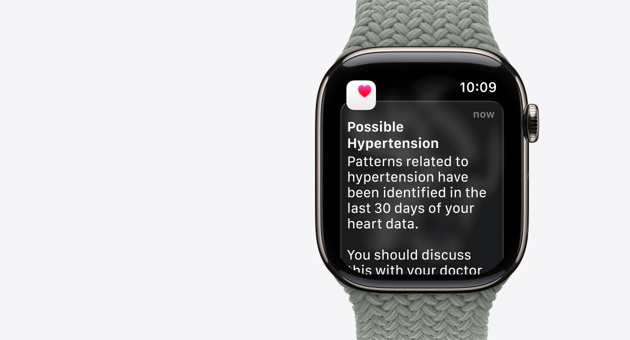 Apple Watch Series 11, titanboett i guldfinish, varning om möjligt högt blodtryck, rosa hjärta i en vit ruta, höger utsida, Digital Crown, armband, grågrön flätad sololoop
