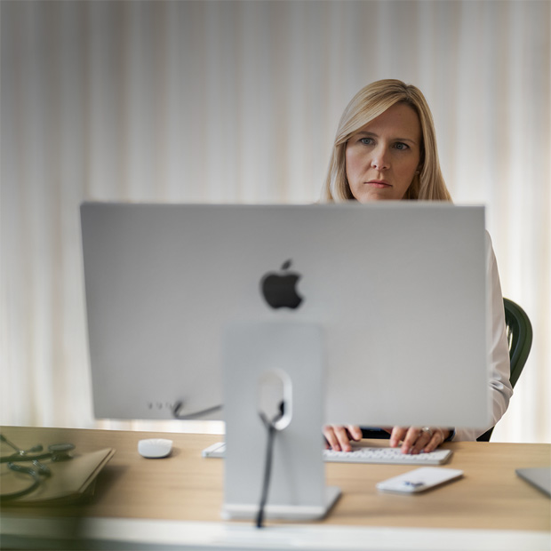 Profissional da saúde olha para a tela do iMac em sua mesa.